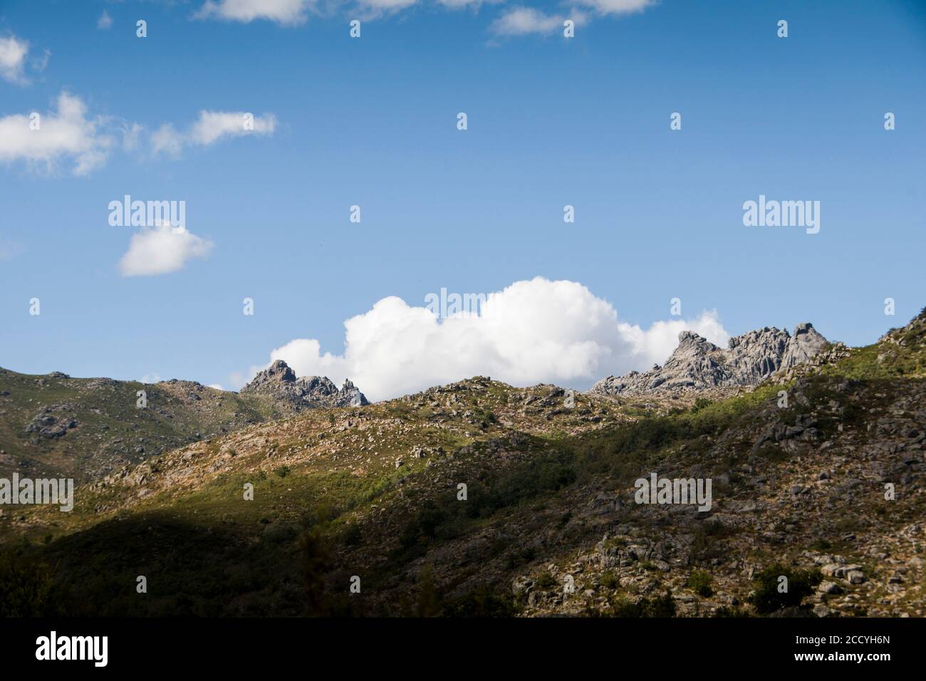 Rocky mountain range formations stand in the horizon view, under blue sky and white clouds. Serene mountain landscape Stock Photo