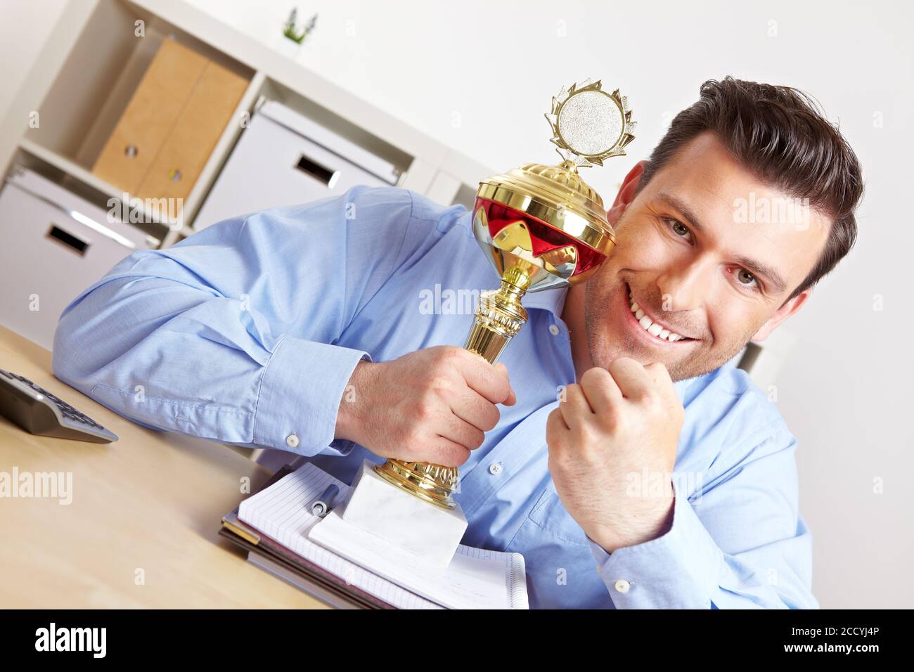 Cheering manager with cup in the office and clenched fist Stock Photo ...