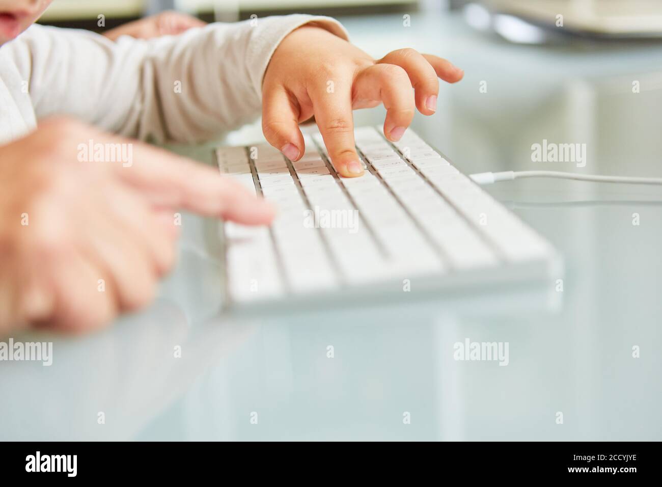 Hand of father helping toddler to type on keyboard on computer Stock