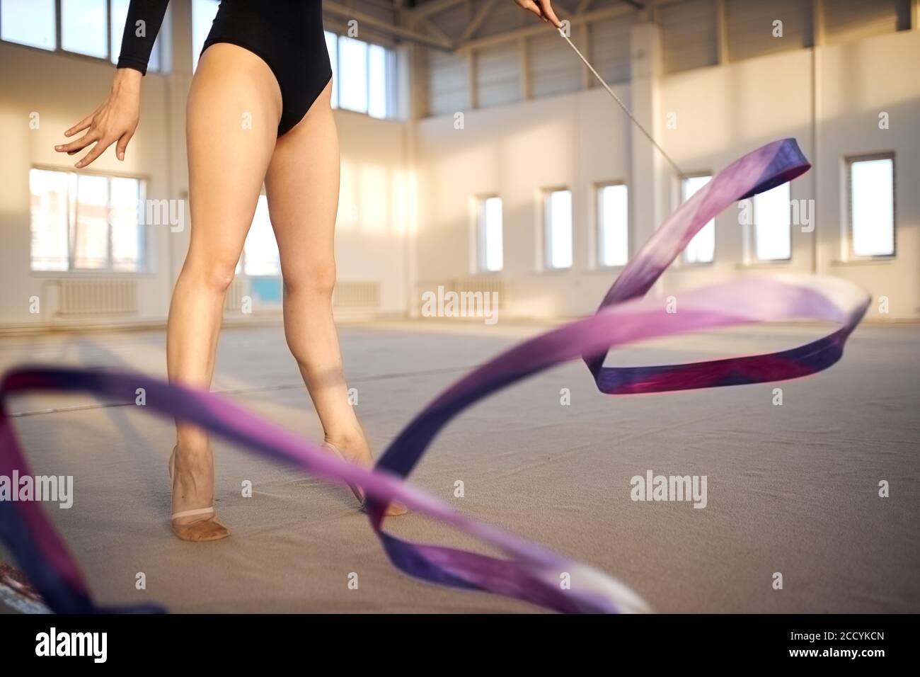 Close view of tall gymnast legs, charming professional gymnast training in roomy gym hall using