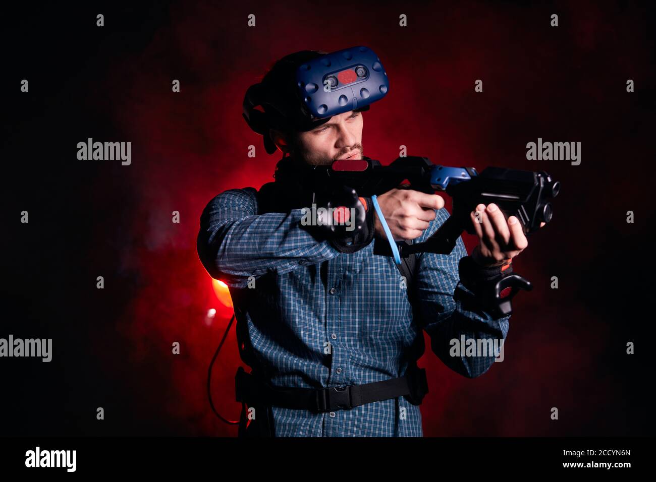 Young male wearing special devices for virtual reality games, isolated over red smoky background. Hi-tech Stock Photo