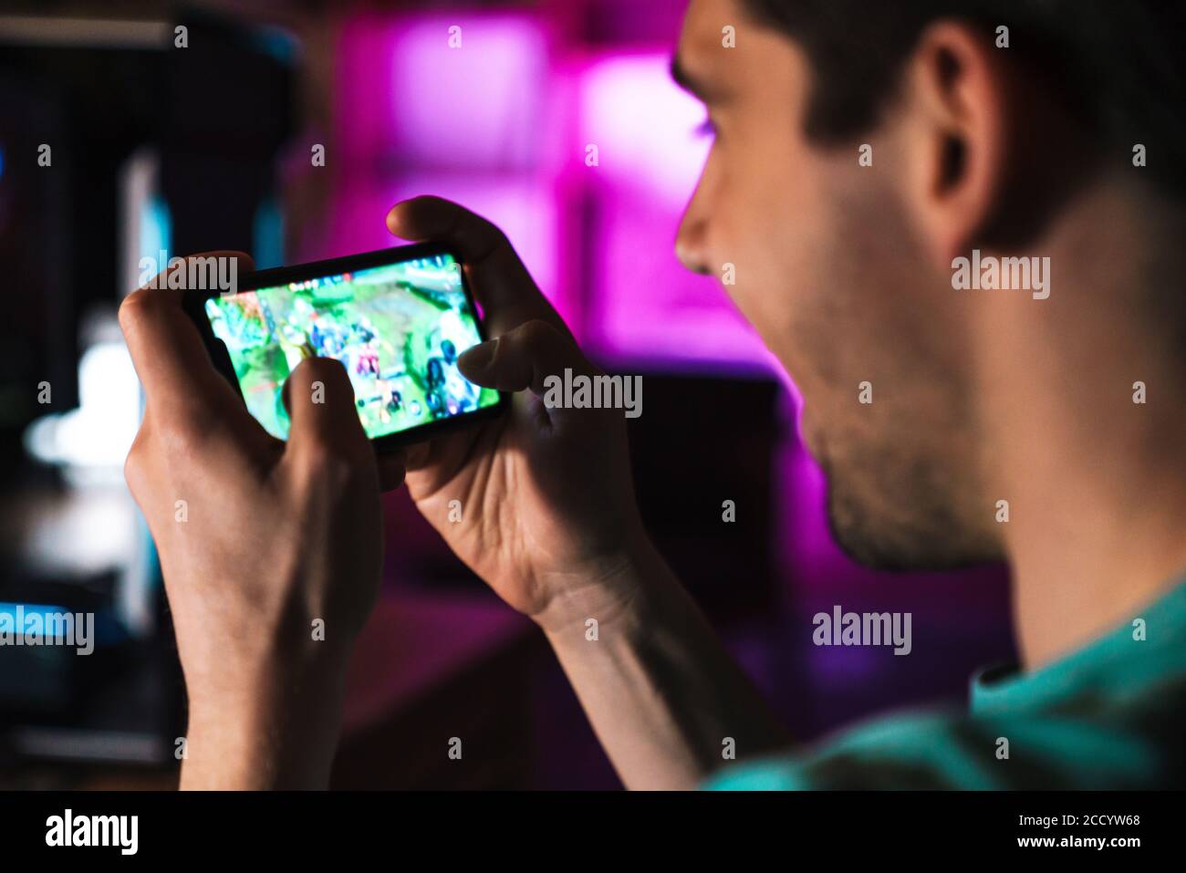 Image closeup of smiling man playing video game on mobile phone and computer at home Stock Photo