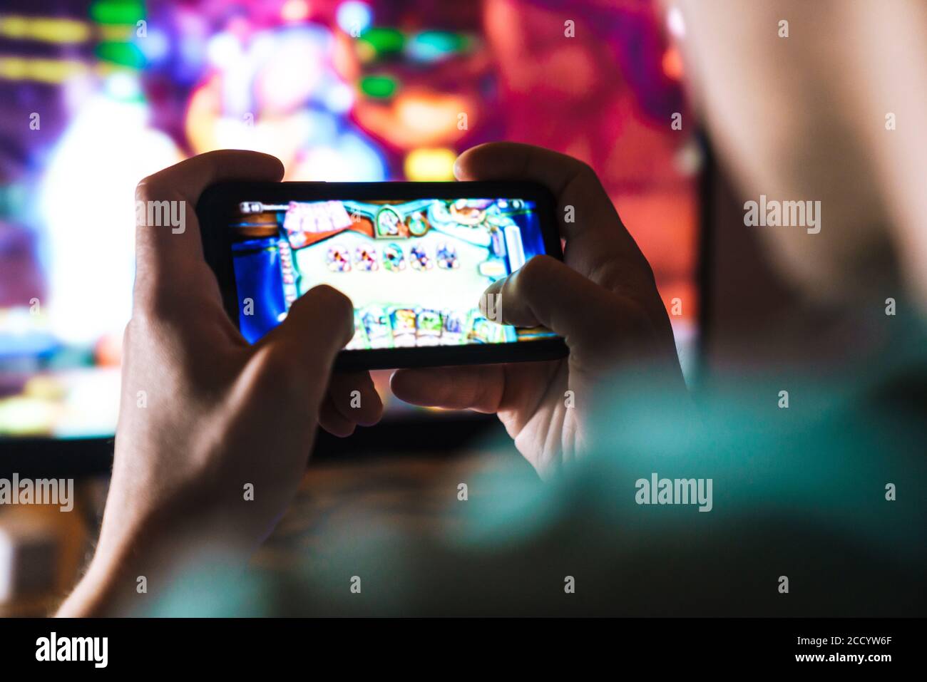 Image closeup of focused man playing video game on mobile phone and computer at home Stock Photo
