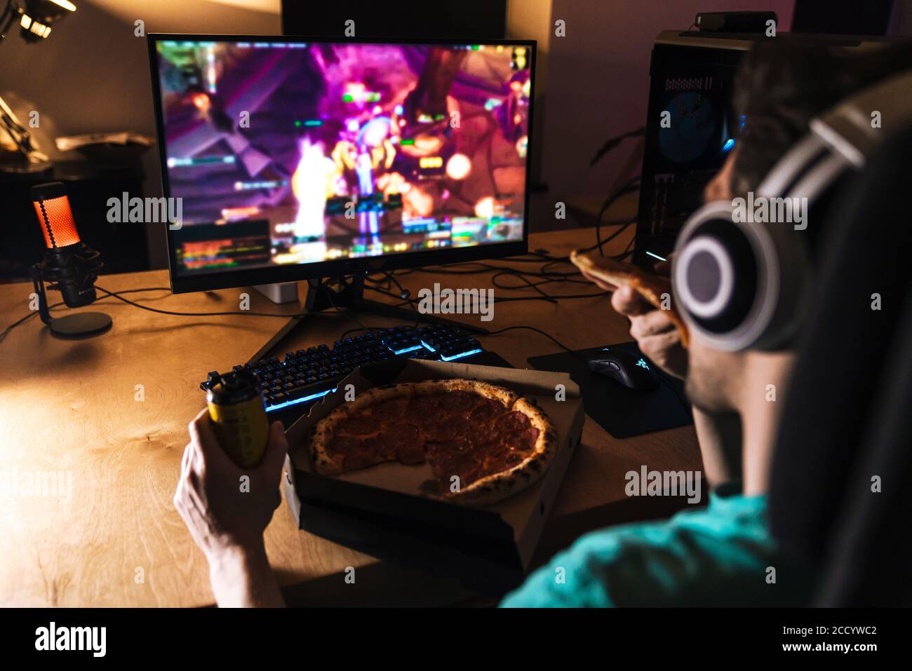 Image of focused young man in headphones eating pizza while playing
