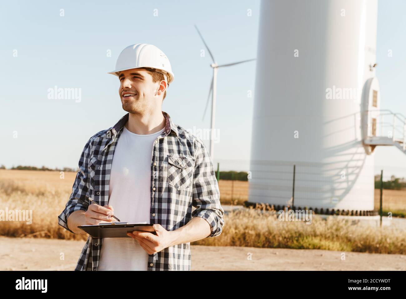 An electrical engineer standing on a field with windmills, taking notes Stock Photo