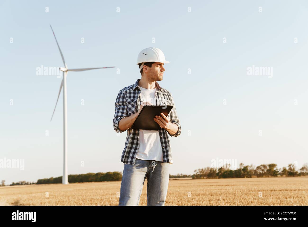 An electrical engineer standing on a field with windmills, taking notes Stock Photo