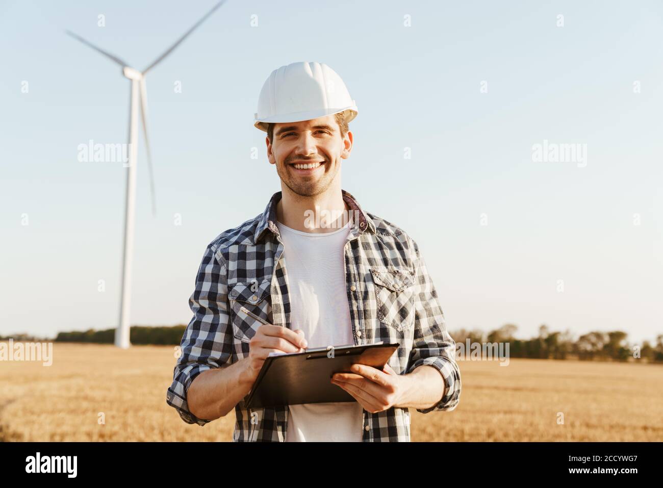 An electrical engineer standing on a field with windmills, taking notes Stock Photo