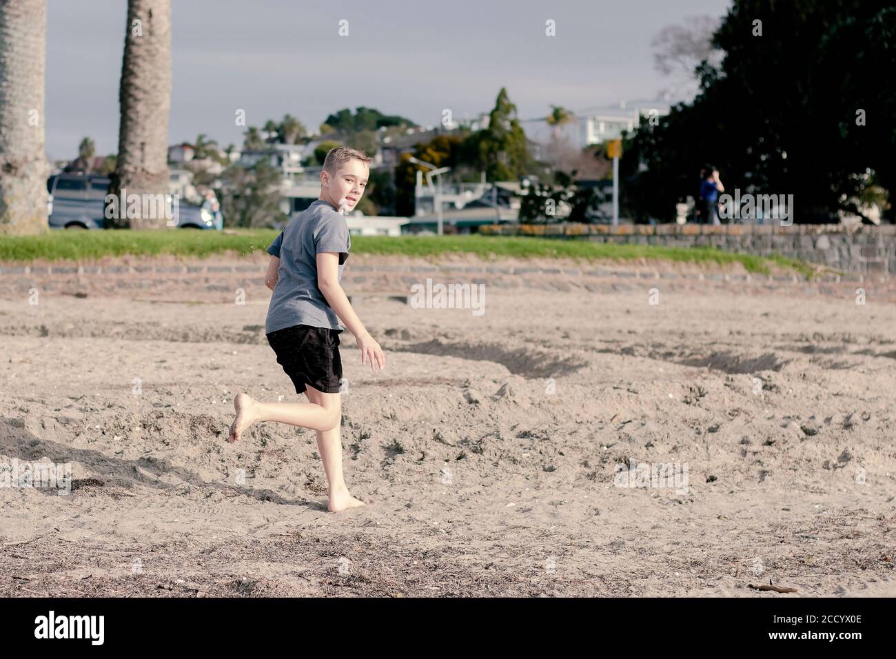 A young boy running on the beach whilst looking backward over his shoulder. Stock Photo