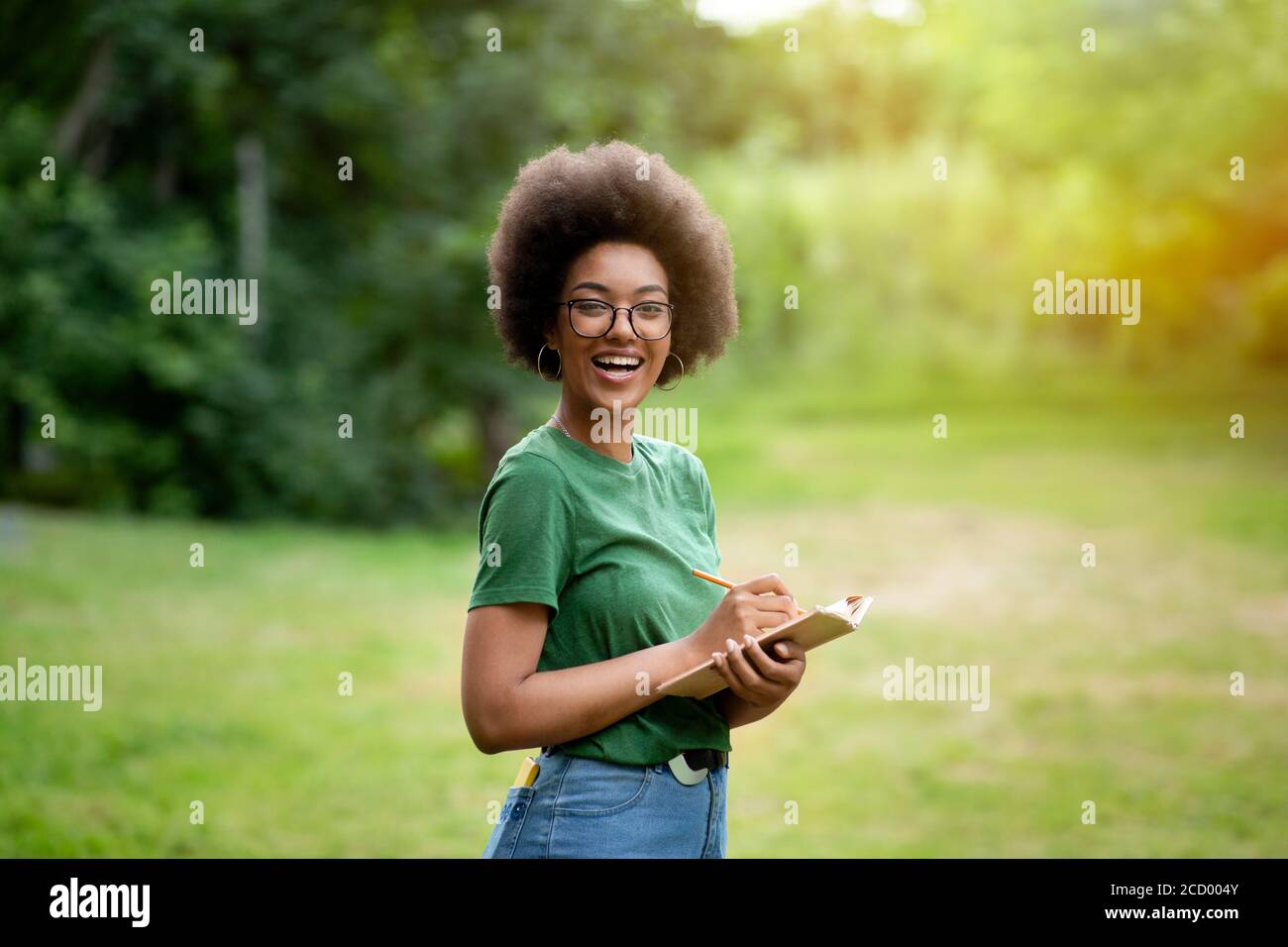 Positive Black Student Girl In Eyeglasses Standing Outdoors Taking Notes To Notepad Stock Photo