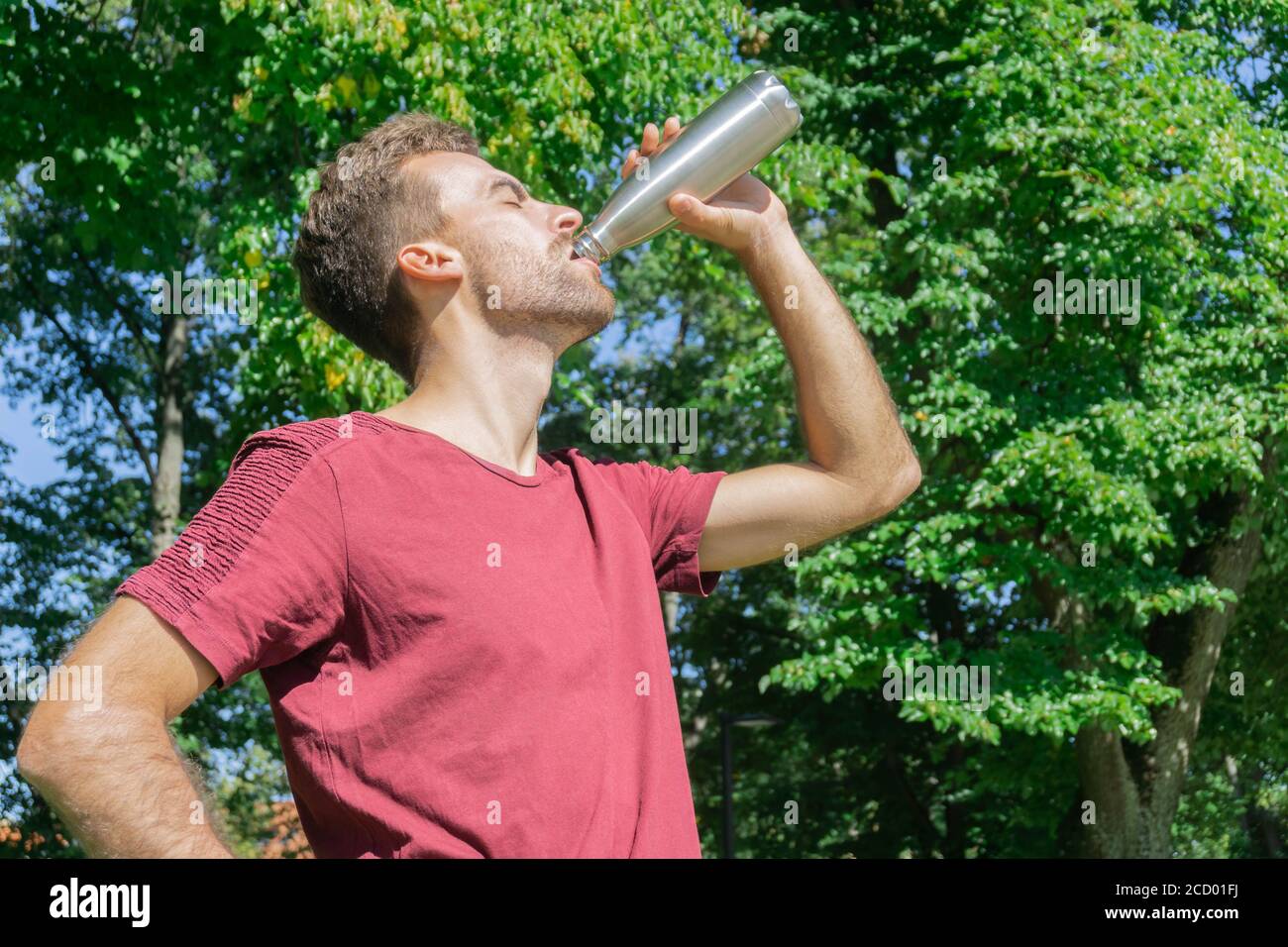 Man drinking water in trees foliage background. Thirsty guy drinking