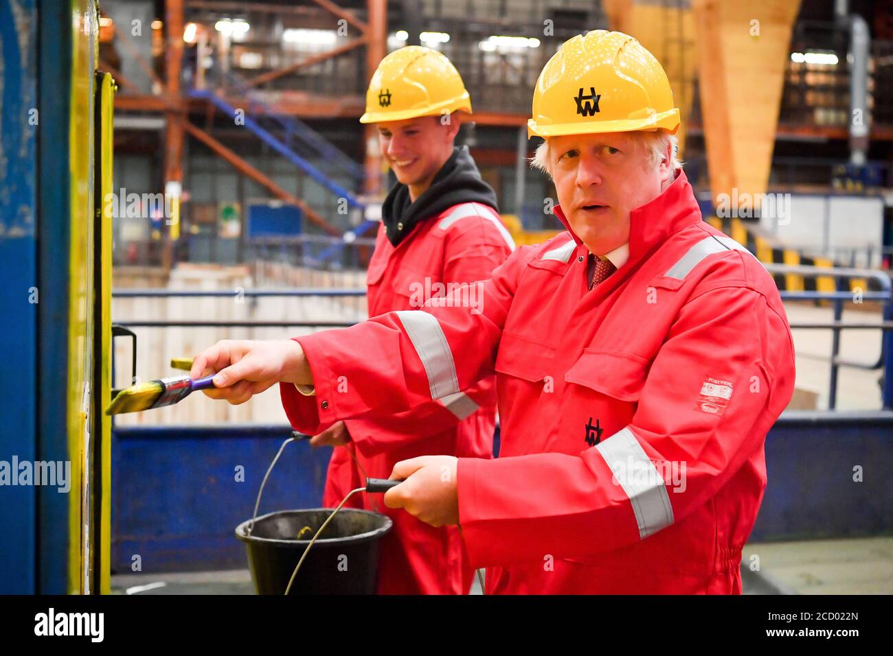 Prime Minister Boris Johnson helps contractor Sam Evans, 20, to paint machinery yellow during
