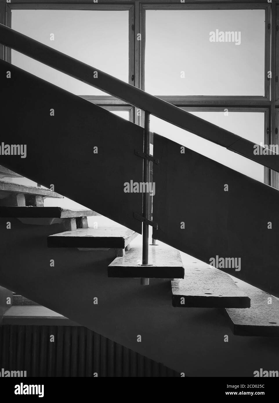 Black and white interior architecture details, old staircase by the window. Wooden railing and stone stair steps inside a shabby building. Aged constr Stock Photo