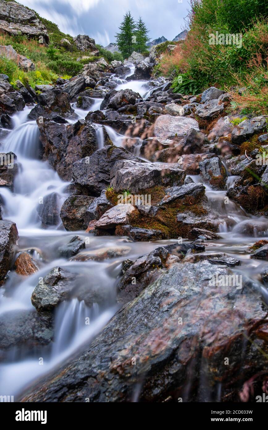 Waterfall flowing down a rocky mountain slope in the Italian Alps near Ruscello, Livigno, Lombardy in a long exposure looking up the ravine Stock Photo