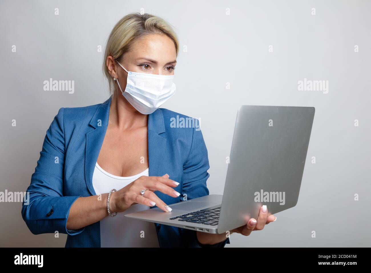 young blonde in a medical mask, in a blue jacket with a laptop in her hands. Self-isolation concept during coronavirus, Remote tabot, education, online communication. High quality photo Stock Photo