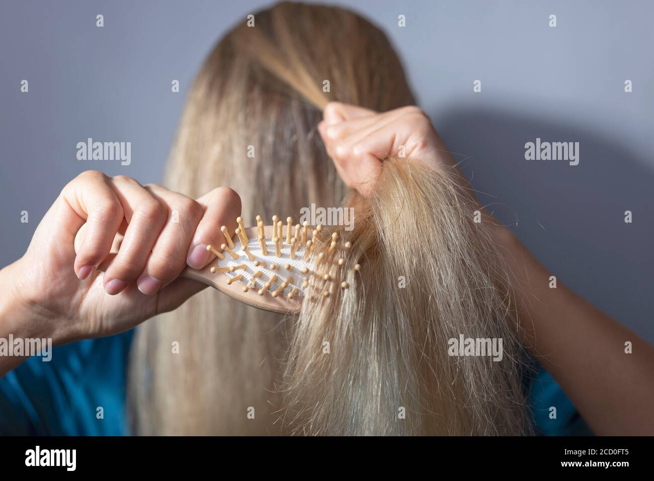 blonde combs dry hair with a wooden comb. On a gray background. Hair