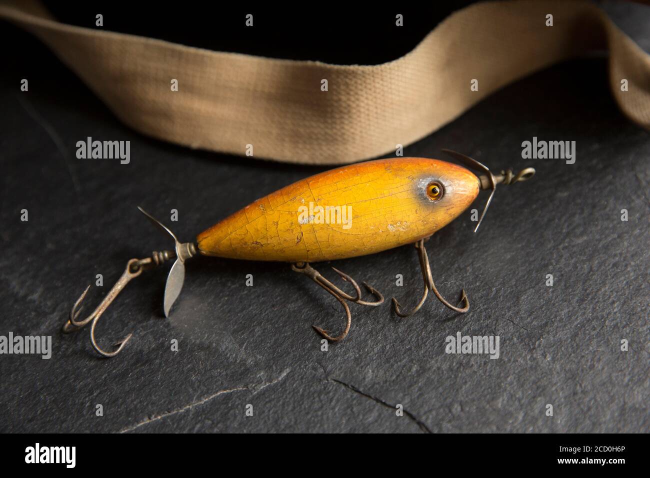 An example of an old South Bend fishing lure, or plug, designed to catch predatory fish displayed on a dark slate background next to an old whicker ta Stock Photo