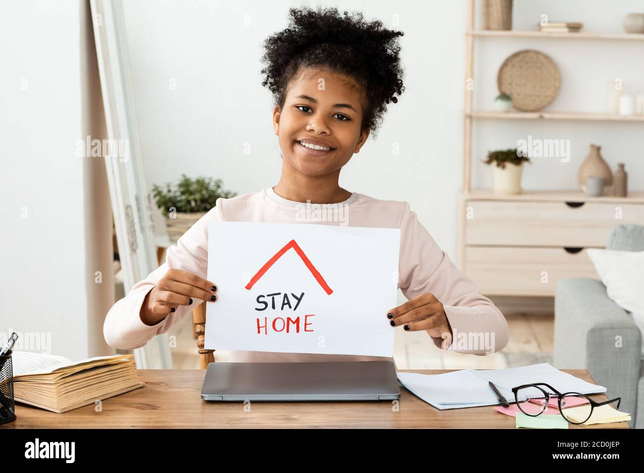 Black School Girl Holding Paper With Stay-At-Home Text Sitting Indoors Stock Photo