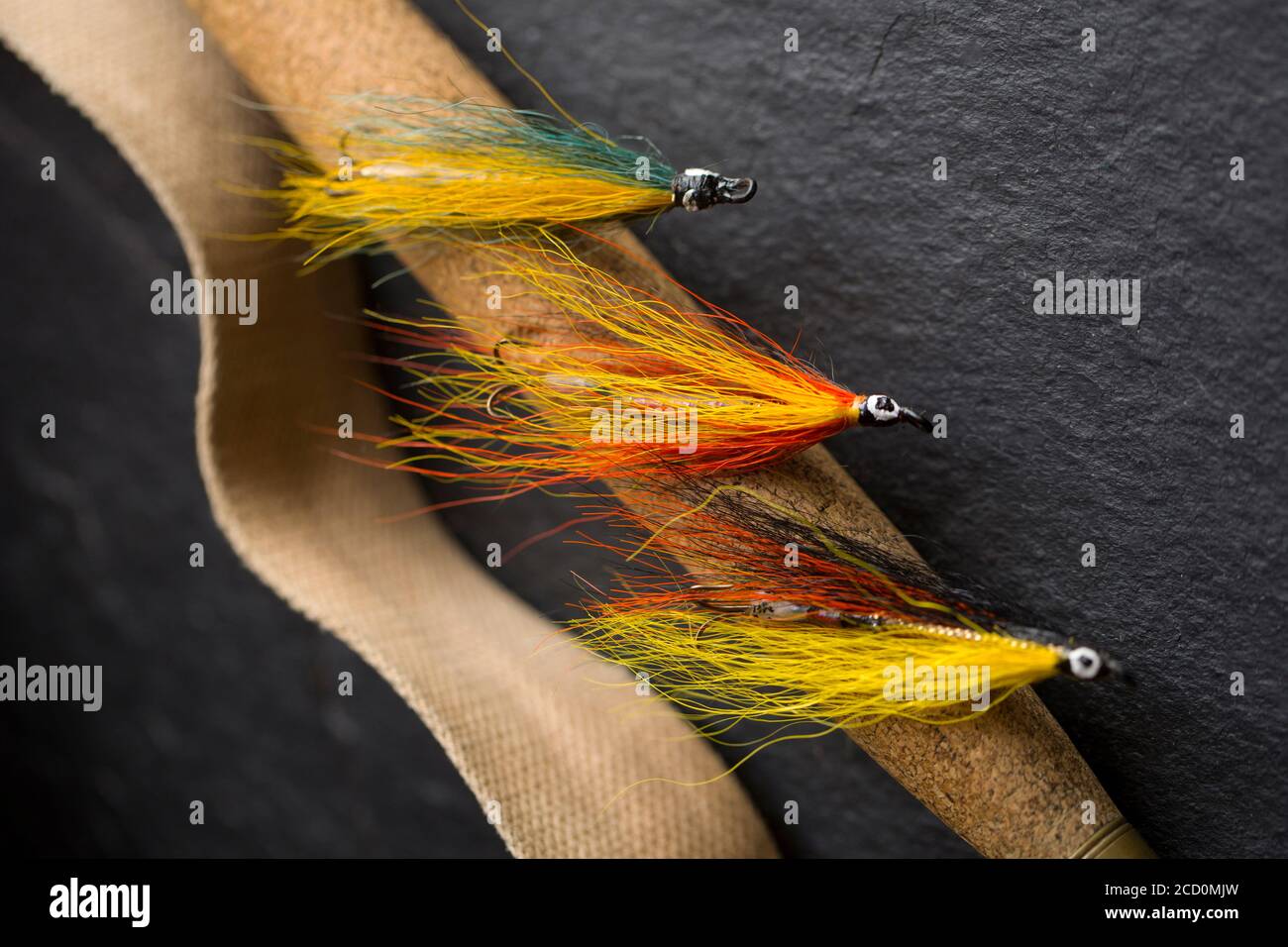 Three salmon flies that were probably homemade on the cork handle of an old  fly fishing rod next to the strap from a whicker tackle box. From a collec  Stock Photo 