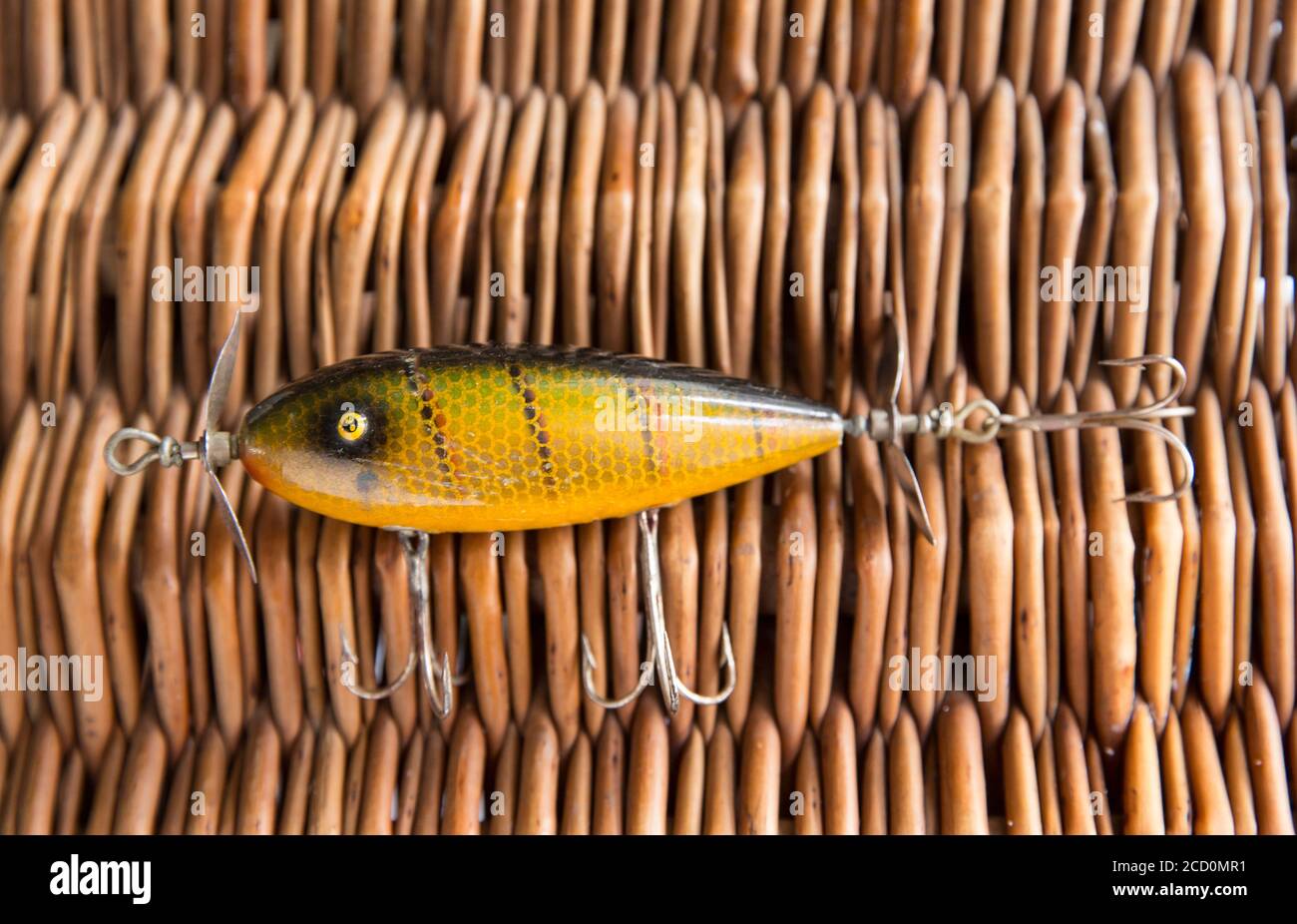 An old South Bend fishing lure, or plug, designed for catching predatory fish photographed against the whicker lid of an old tackle box. From a collec Stock Photo