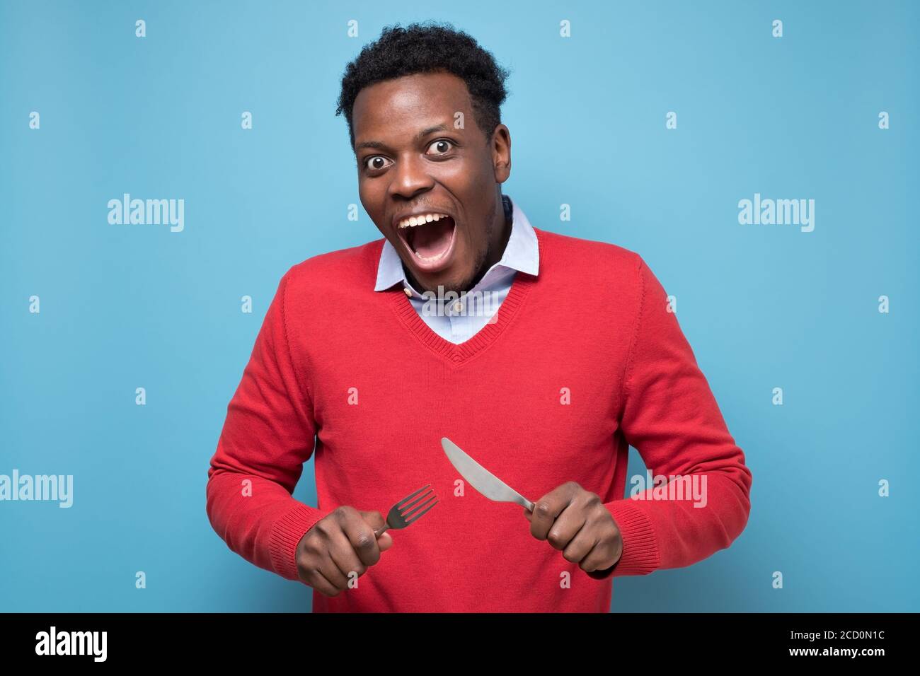 Hungry african man holding fork and knife raised waiting for dinner. Stock Photo