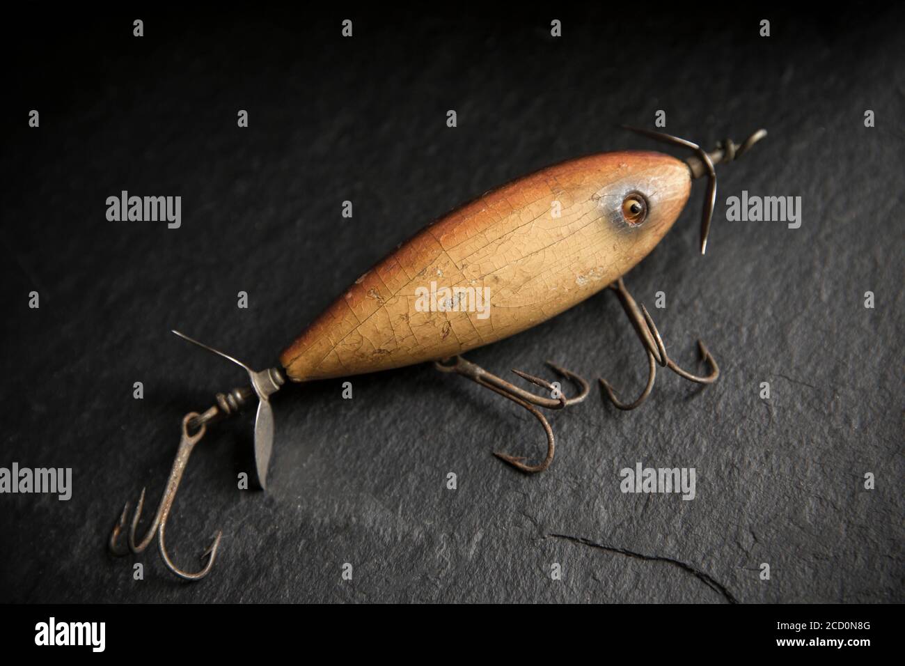An example of an old South Bend fishing lure, or plug, designed to catch predatory fish displayed on a dark slate background. Desaturated colours. Fro Stock Photo