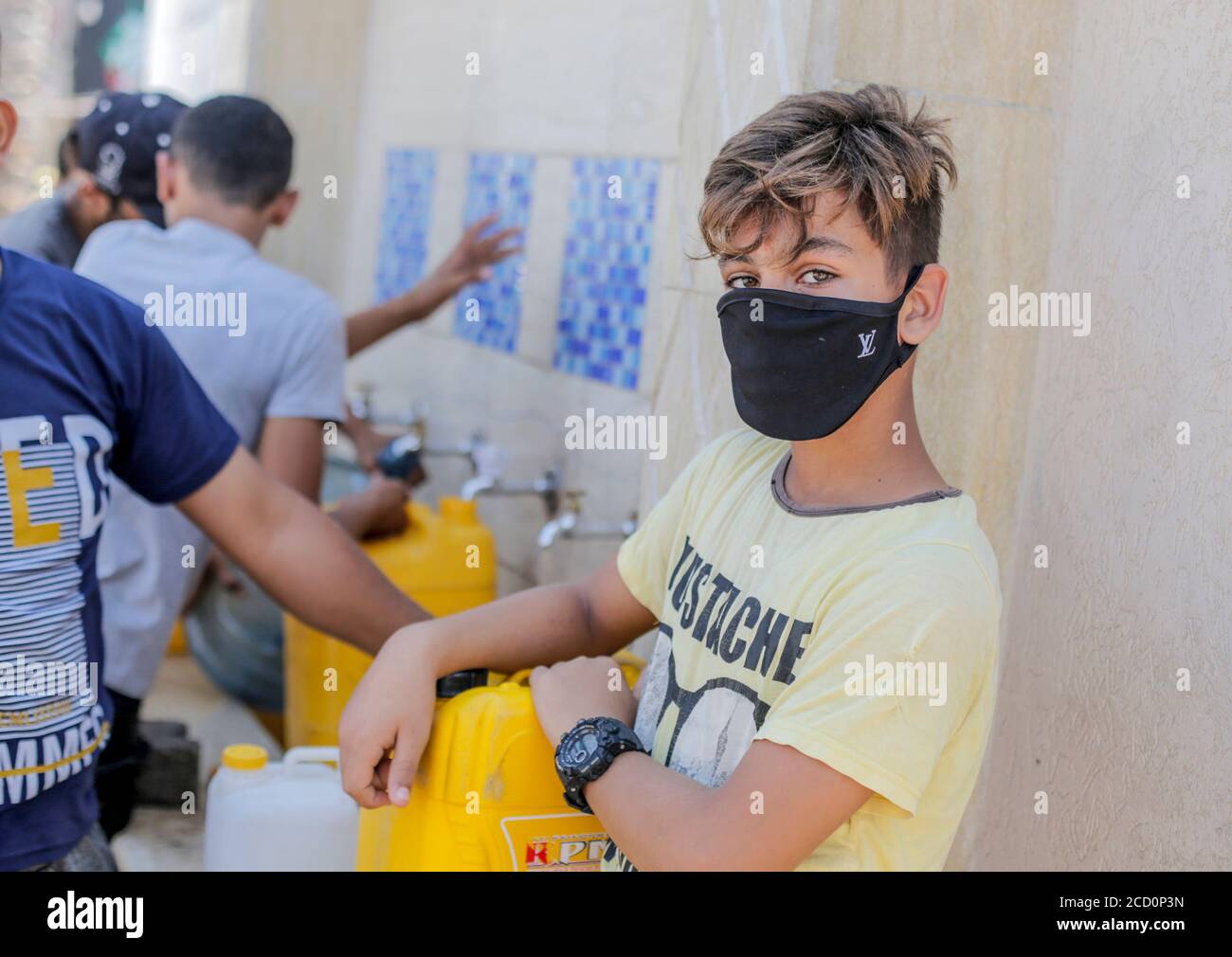 A kid wearing a face mask as a preventive measure waits to fill bottles with drinking water from a desalination plant during the Coronavirus (COVID-19) lockdown .Gaza reported its first cases in the general population as authorities confirmed four infections at a refugee camp and security forces declared a full lockdown for 48 hours. The four cases were from a single family, according to a government statement. The closure would affect the entire Gaza Strip, according to an official from Hamas, the group that governs the territory. Stock Photo