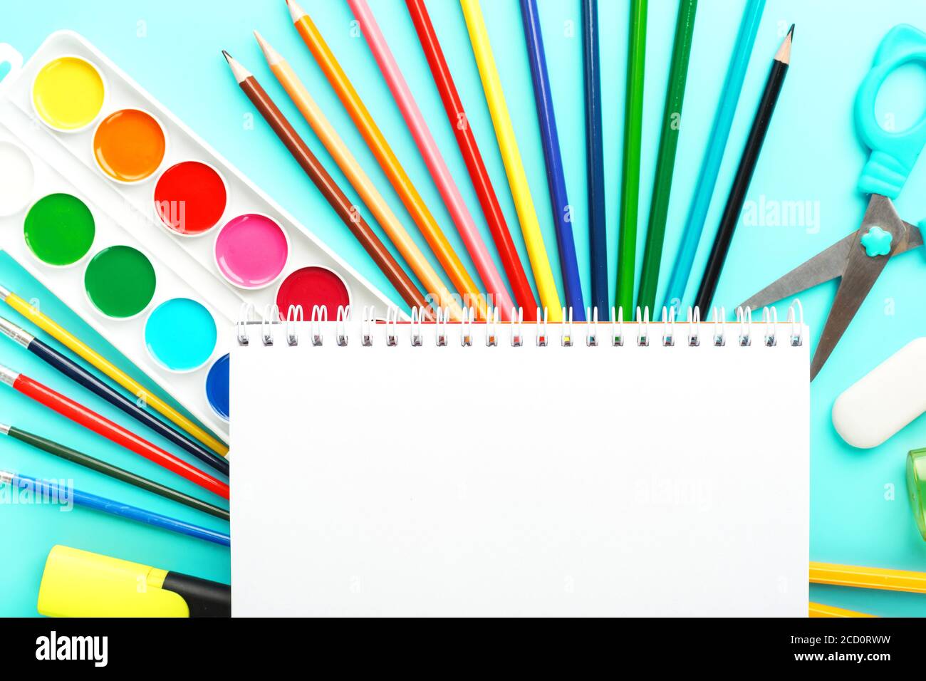 An album for creative development at school, with stationery on a cyanide background. A palette of colored paints, markers, brushes and pencils. Stock Photo