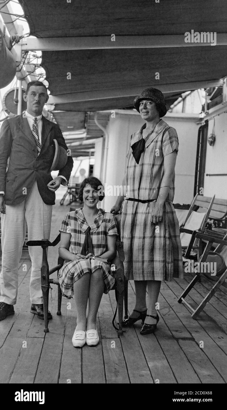 A vintage 1920s black and white photograph showing a family, father, Mother, and daughter, posing on the deck of a steam ship. They show the typical fashion of the period. Stock Photo
