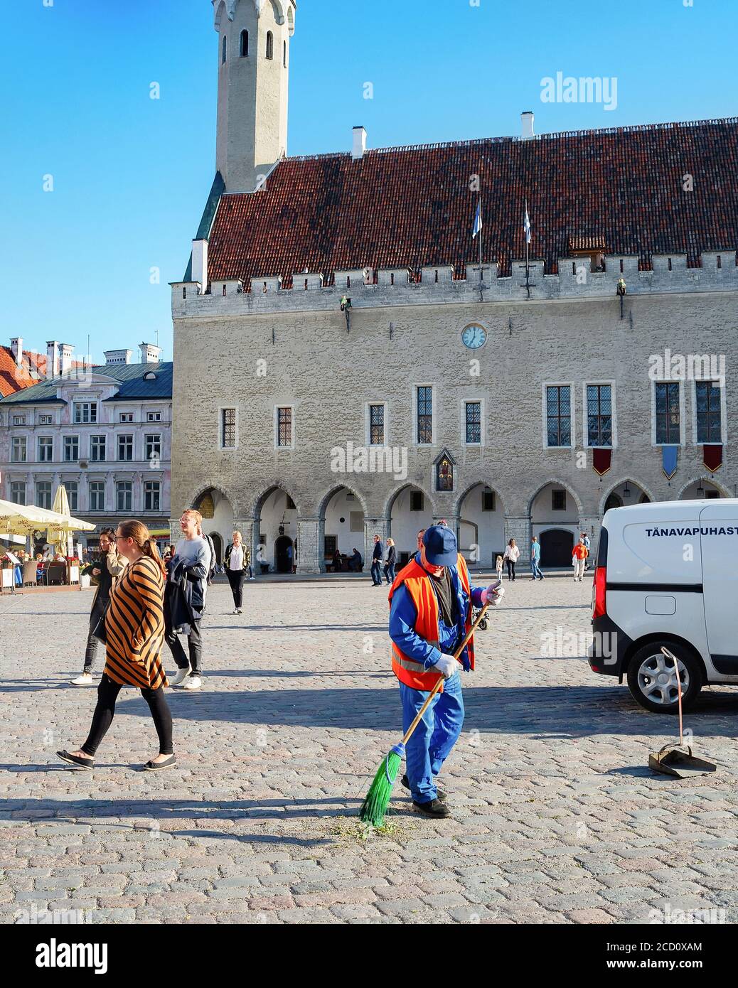 TALLINN, ESTONIA - JULY 14, 2019: Man sweeping central Town Hall Square, walking tourists, old town cityscape in bright sunlight Stock Photo