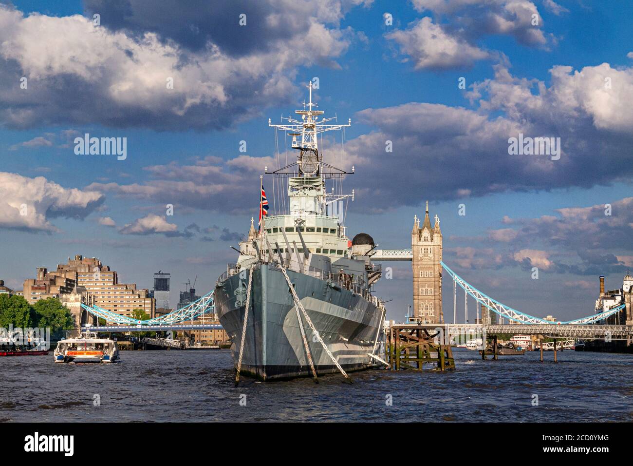 HMS Belfast museum ship moored on River Thames with The Tower Thistle Hotel London,& a passing RB1 River Clipper Boat with Tower Bridge behind London SE1 Stock Photo