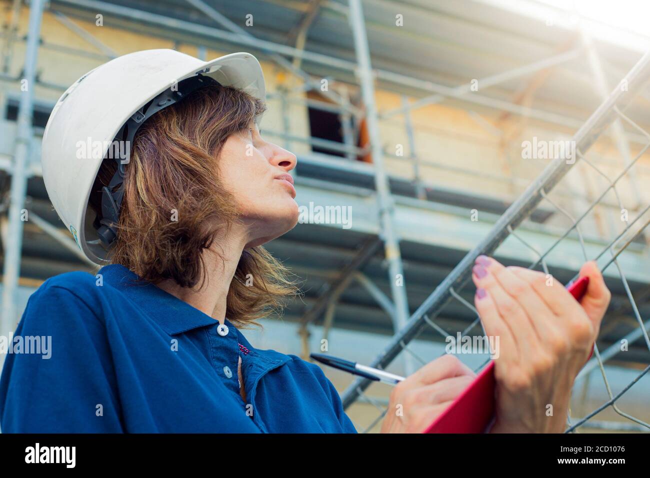 Woman, female engineer, caucasian, age 40, wearing a safety white cap, working on a costruction site in a typical men's role. Gender gap symbol. Stock Photo