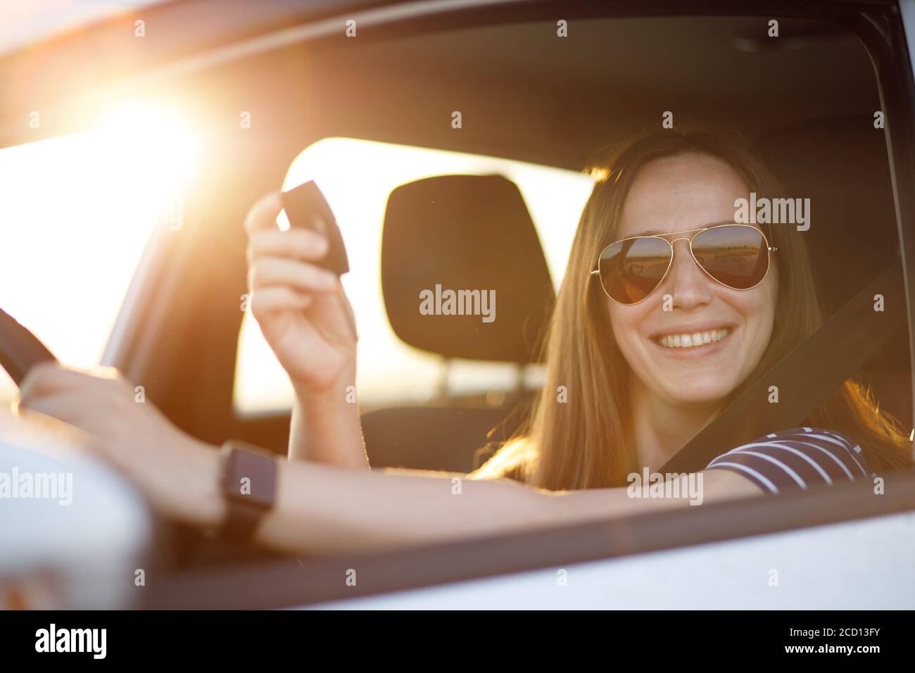 Portrait of young driver woman hold key of rented or new car in sunset beams Stock Photo