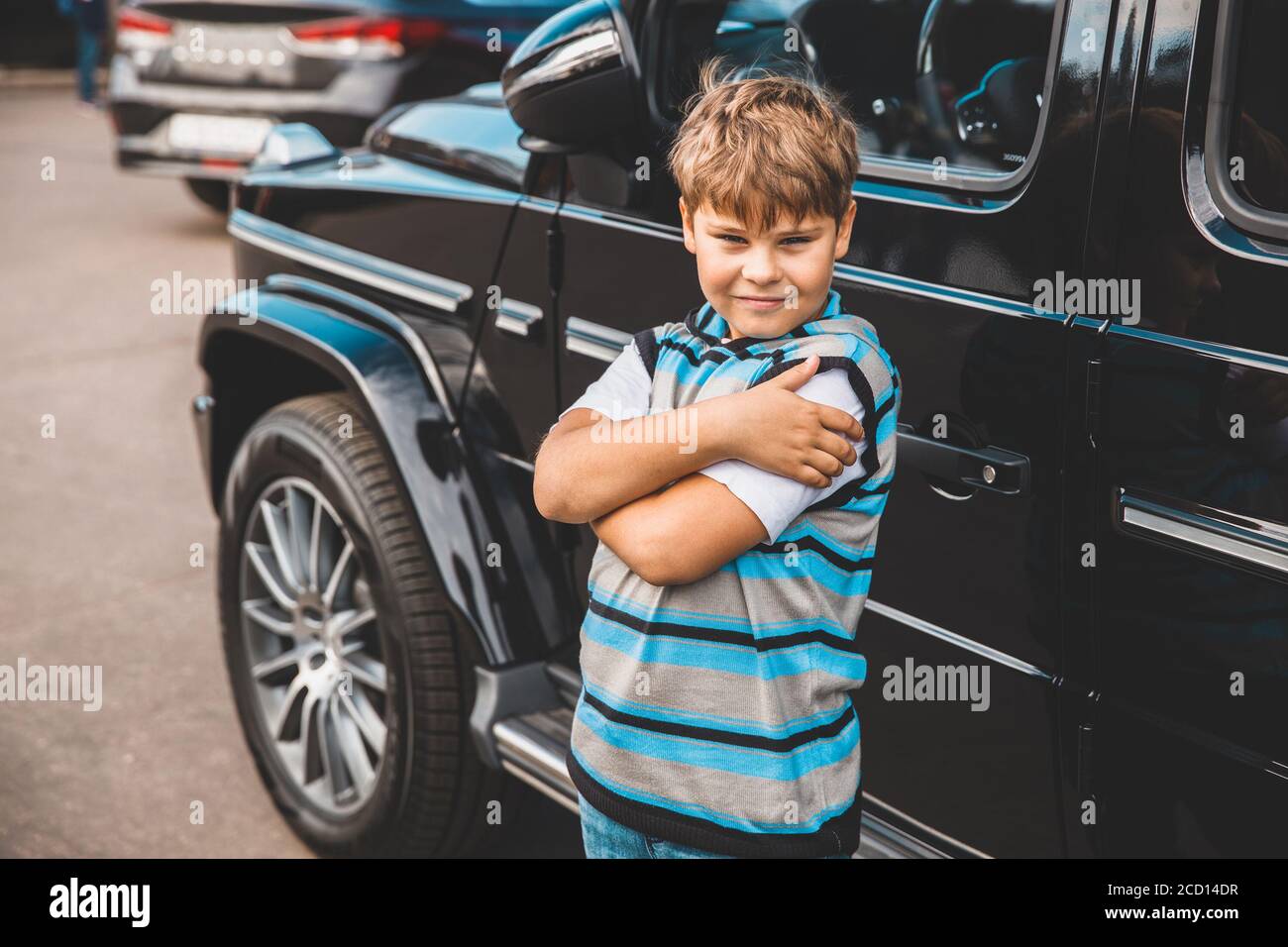 a young boy in a striped sweater stands next to a car Stock Photo - Alamy