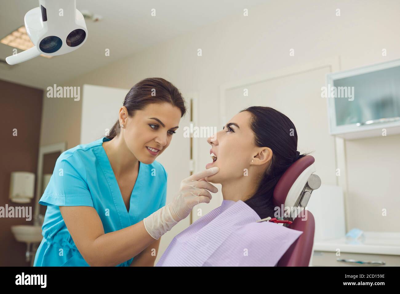 Woman doctor dentist looking at open woman patients mouth and examining
