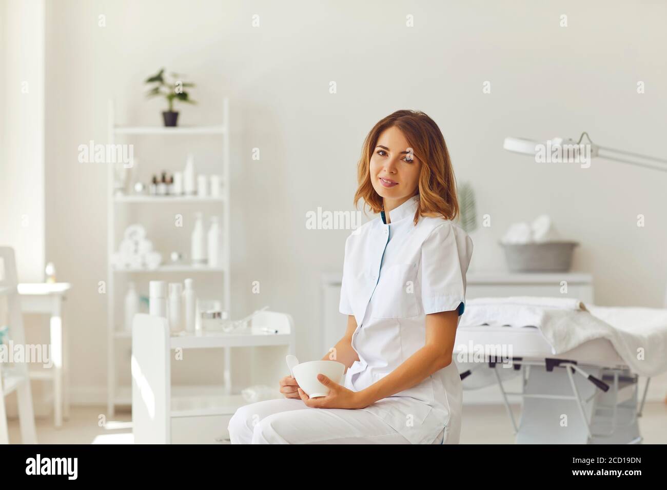 Woman beautician sitting in a beauty salon. Beautician in the white office of the cosmetology clinic. Stock Photo