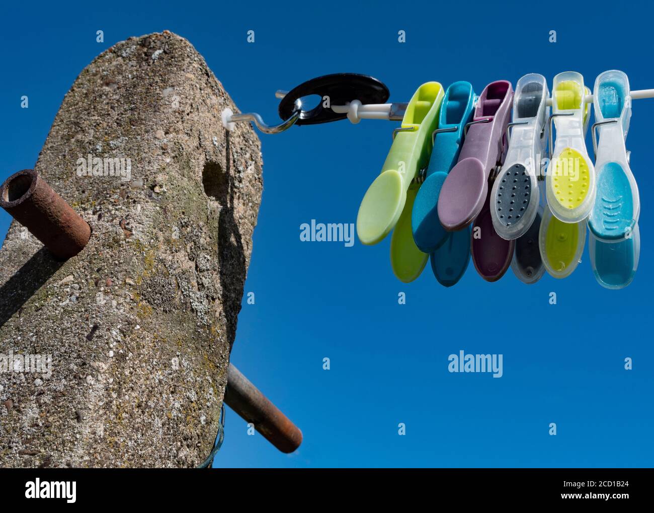 Washing line attached to a hook in a concrete post in a garden / yard, with some colourful pegs