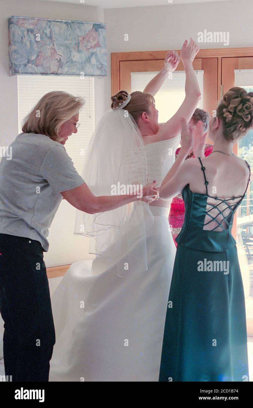 Mother and Bridal Attendants Assist Young Bride with her Wedding Gown before the Ceremony, USA Stock Photo