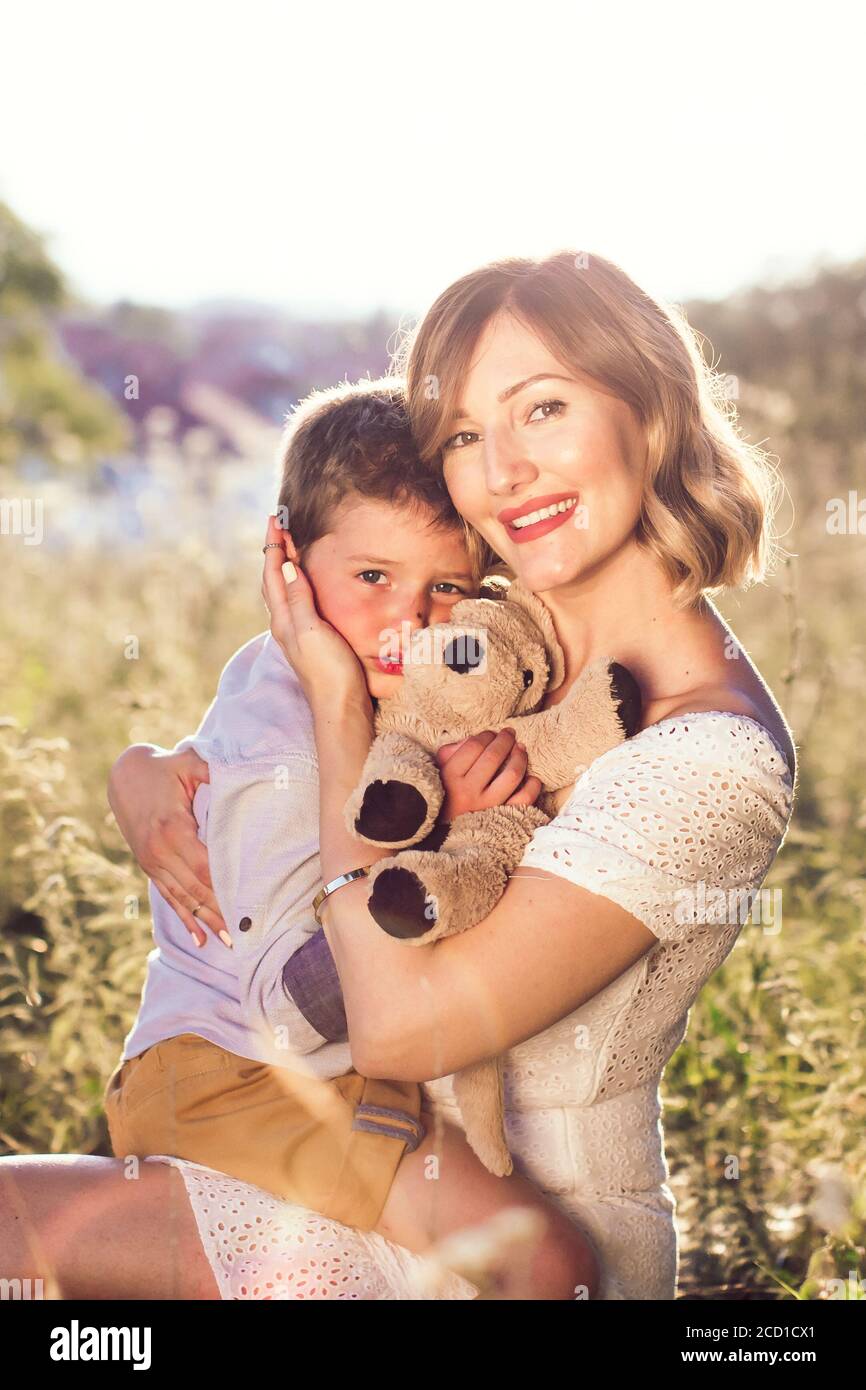 Beautiful young mom holding her blond son in her arms. Outdoor photo. Mothers day Stock Photo