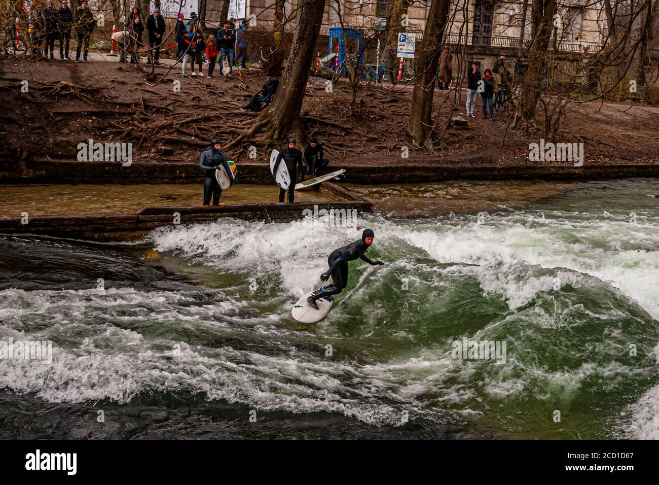 River-Surfing on the Eisbach in Munich, Germany. The standing wave can be surfed for as long as one's balance holds, and in busy times a queue of surfers forms on the bank Stock Photo