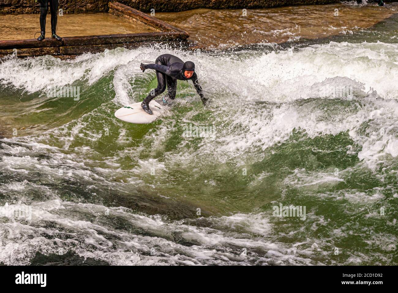 River-Surfing on the Eisbach in Munich, Germany. The standing wave can be surfed for as long as one's balance holds, and in busy times a queue of surfers forms on the bank Stock Photo