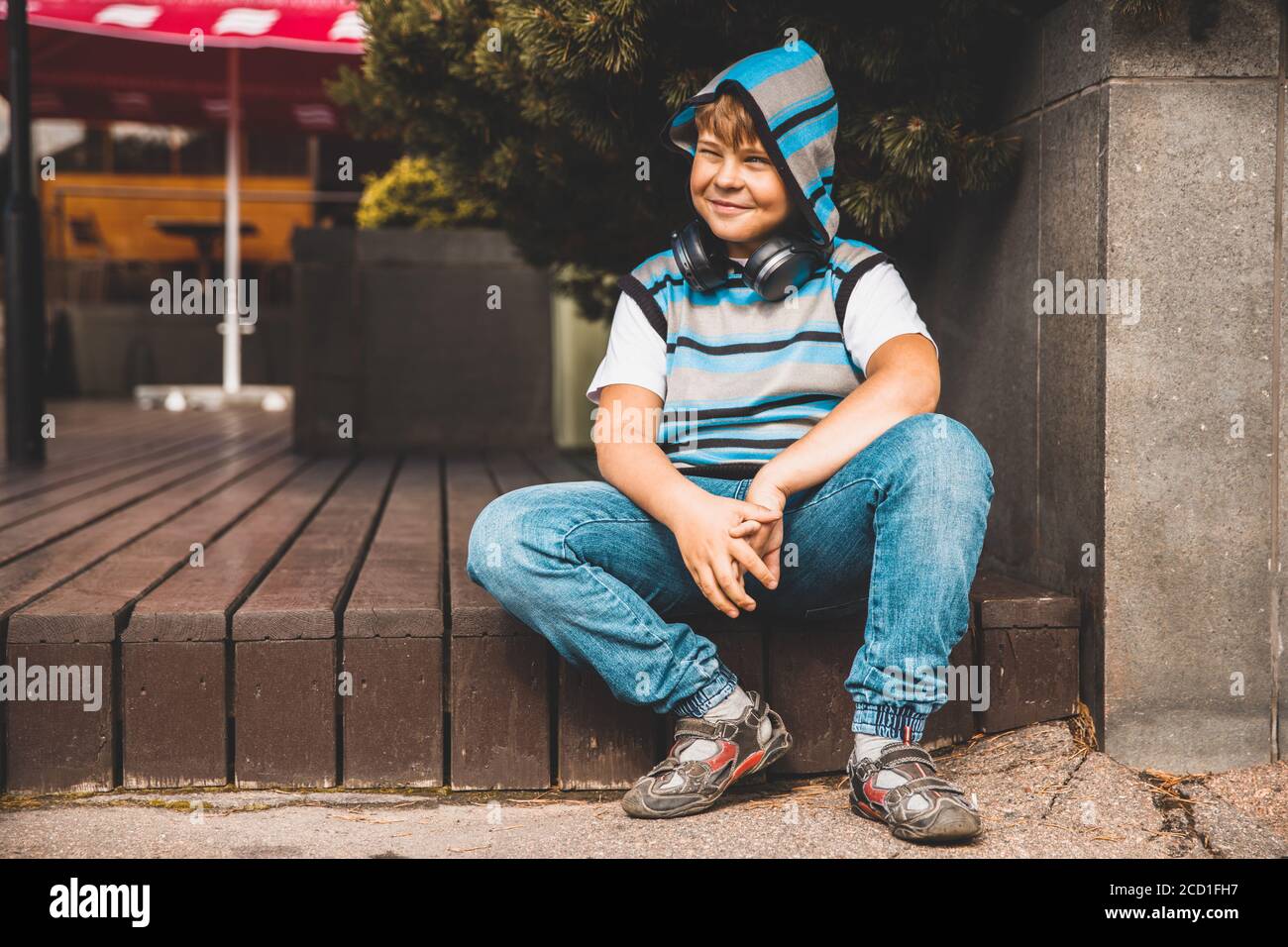 joyful young boy in striped sweater sits on the steps Stock Photo