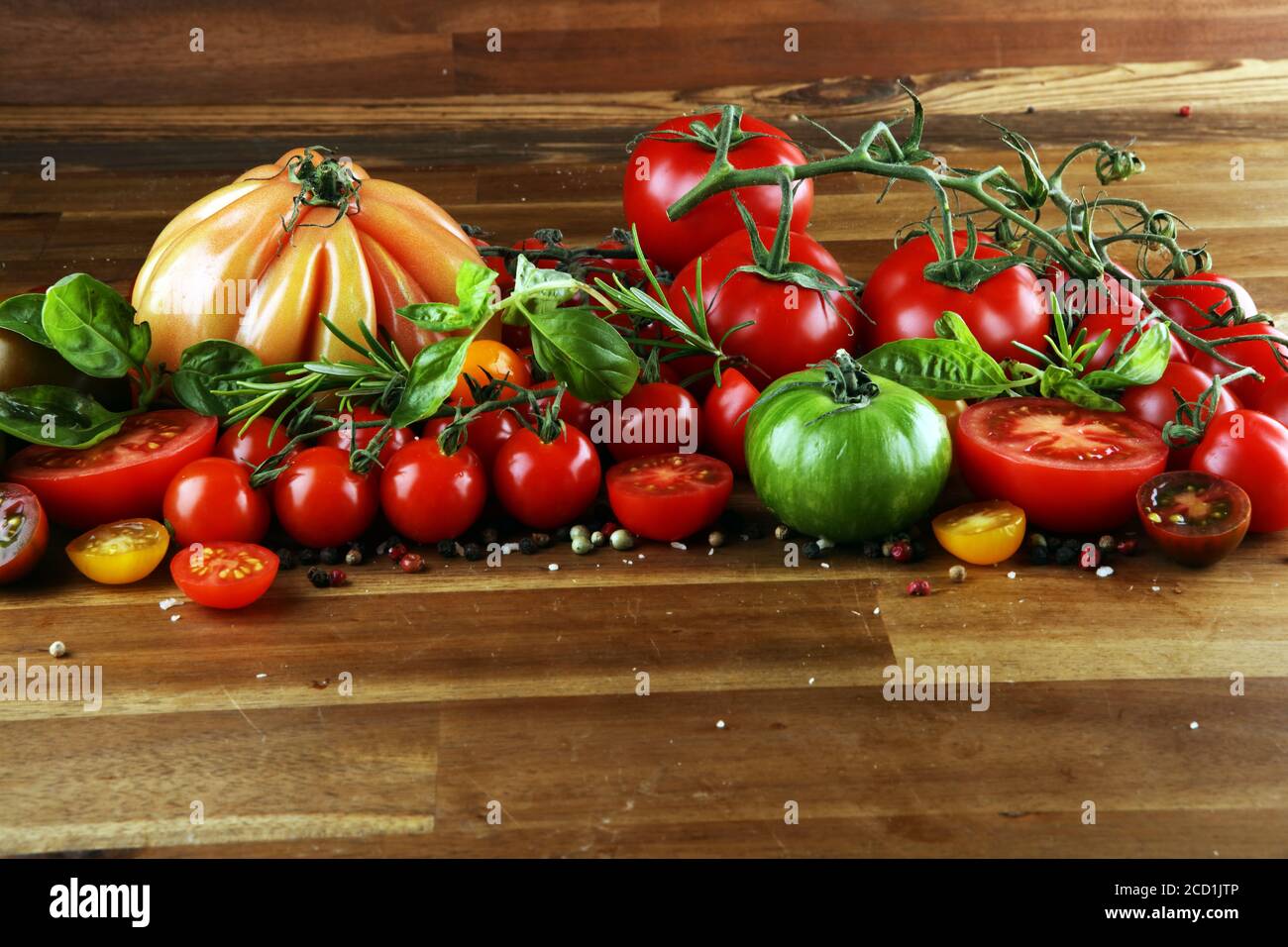 various colorful tomatoes and basil leaves on rustic table. fresh delicious zebra tomato and ccor de boeuf Stock Photo
