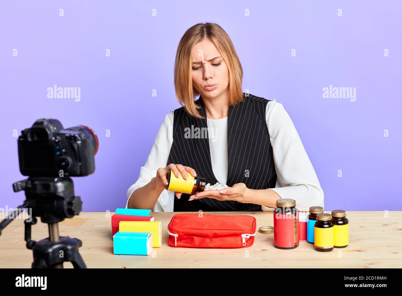 Popular healthcare female consultant prepares new video content about medical kit for her blog, empties out bottle with drugs, handful of pills, thoug Stock Photo