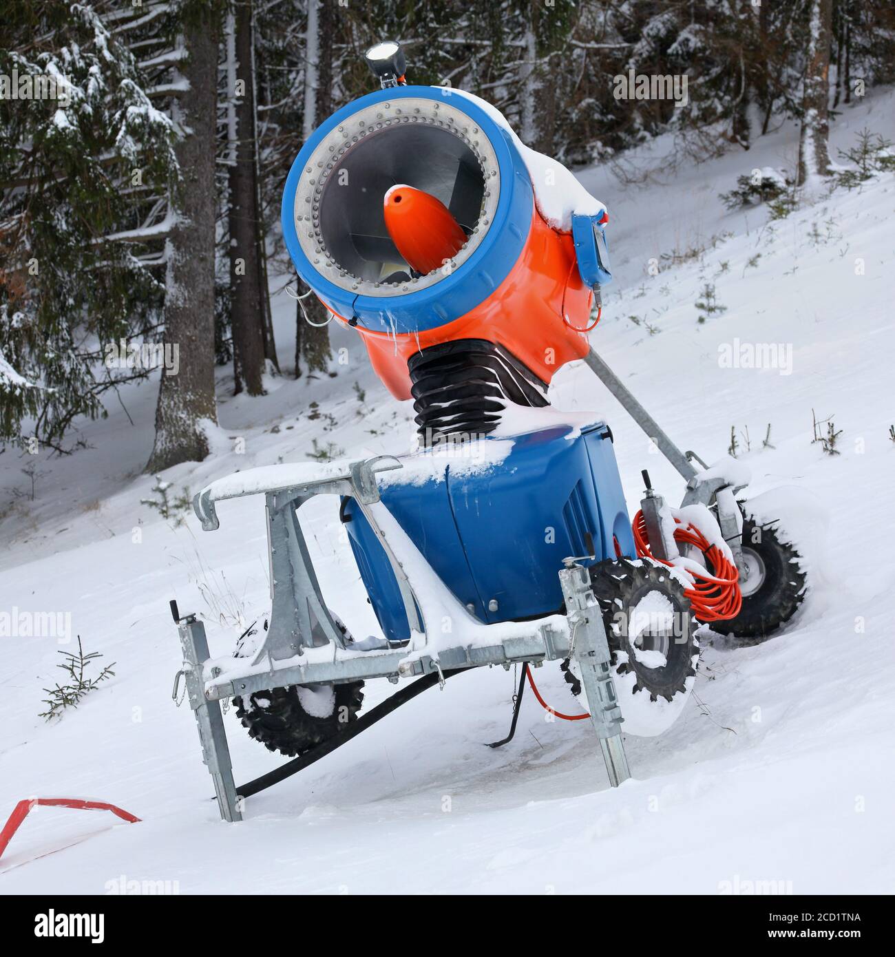 Bright orange and blue snow making cannon, trees in background Stock Photo