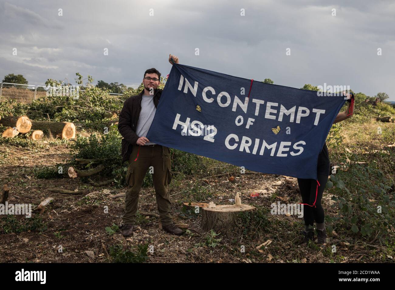 Offchurch, UK. 24th August, 2020. Anti-HS2 activists hold a banner in front of felled trees alongside the Fosse Way. Environmental activists based at wildlife protection camps in Warwickshire have been trying to prevent or delay the felling of large numbers of trees in connection with the £106bn HS2 high-speed rail link, which will destroy or significantly impact many irreplaceable natural habitats including 108 ancient woodlands. Credit: Mark Kerrison/Alamy Live News Stock Photo