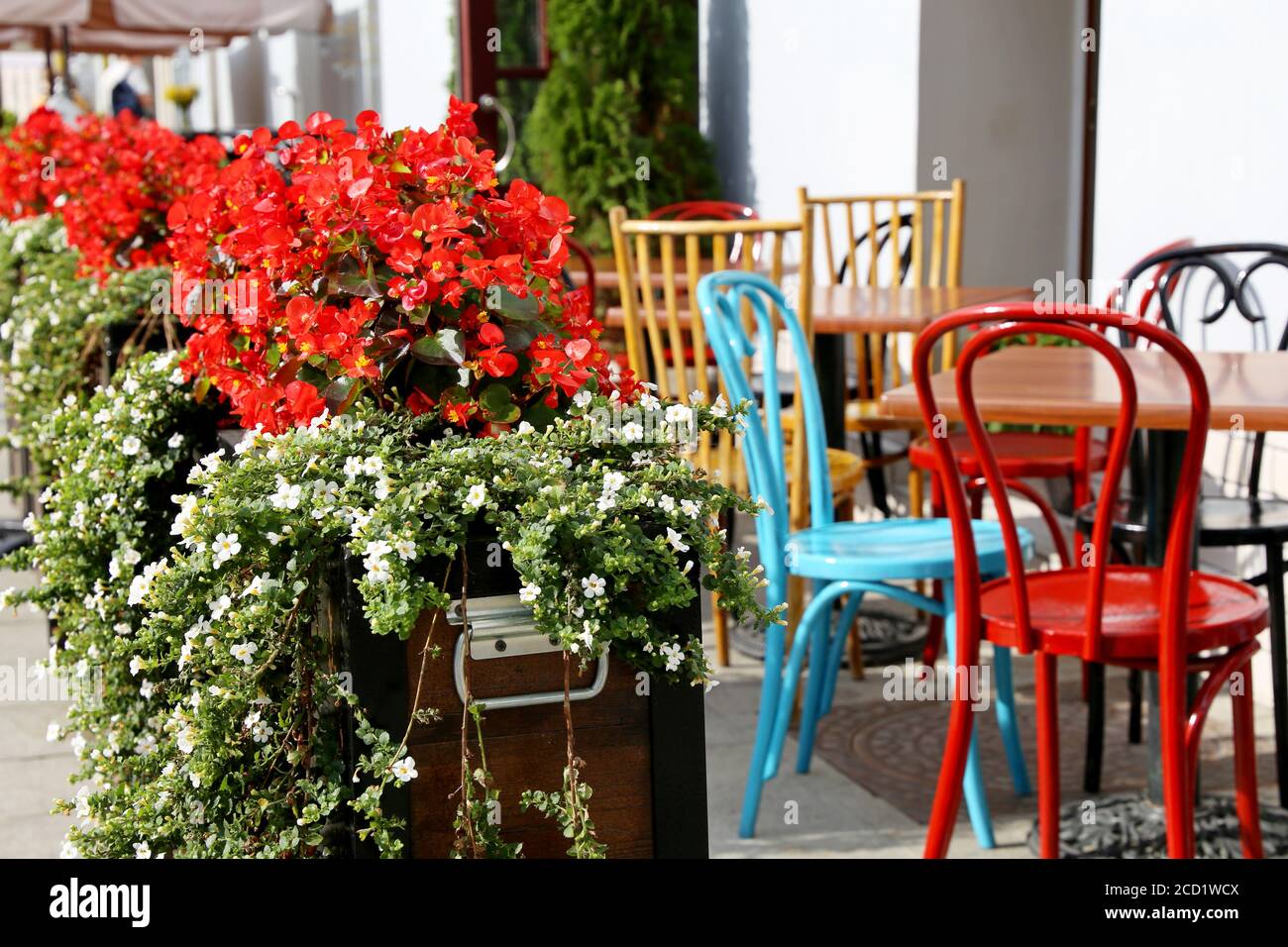 Street cafe in a city, tables and vintage metal chairs in a restaurant outdoor. Pots with flowers, elegant setting for celebration and date Stock Photo