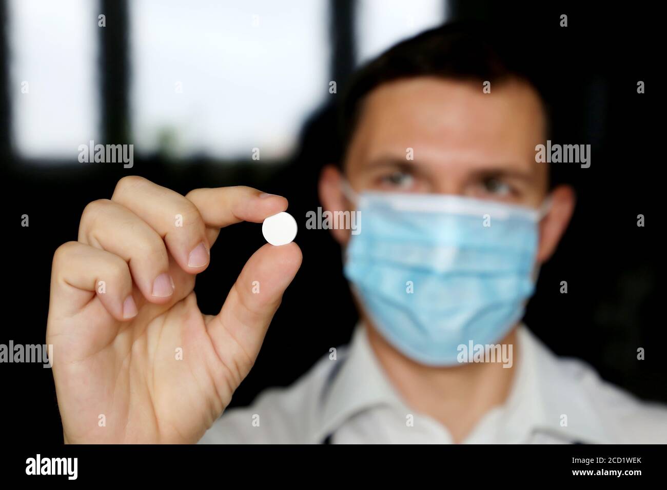 Doctor in medical mask holding white pill, male hand with medication close up. Concept of pharmacist, drugs, antibiotic or vitamin Stock Photo