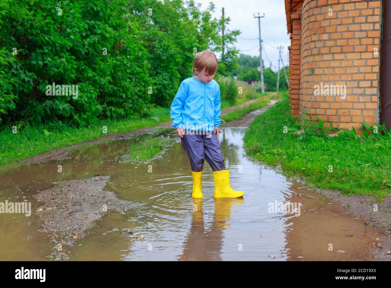 .Child in rubber boots and raincoat playing in a puddle Stock Photo - Alamy