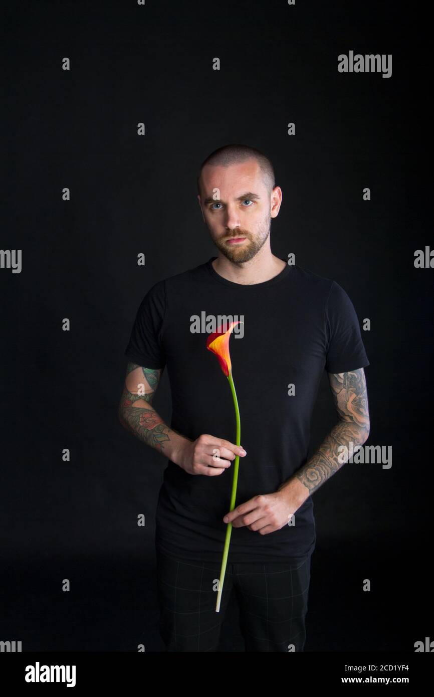Portrait of young man holding single red calla flower on black background, greeting card or concept Stock Photo