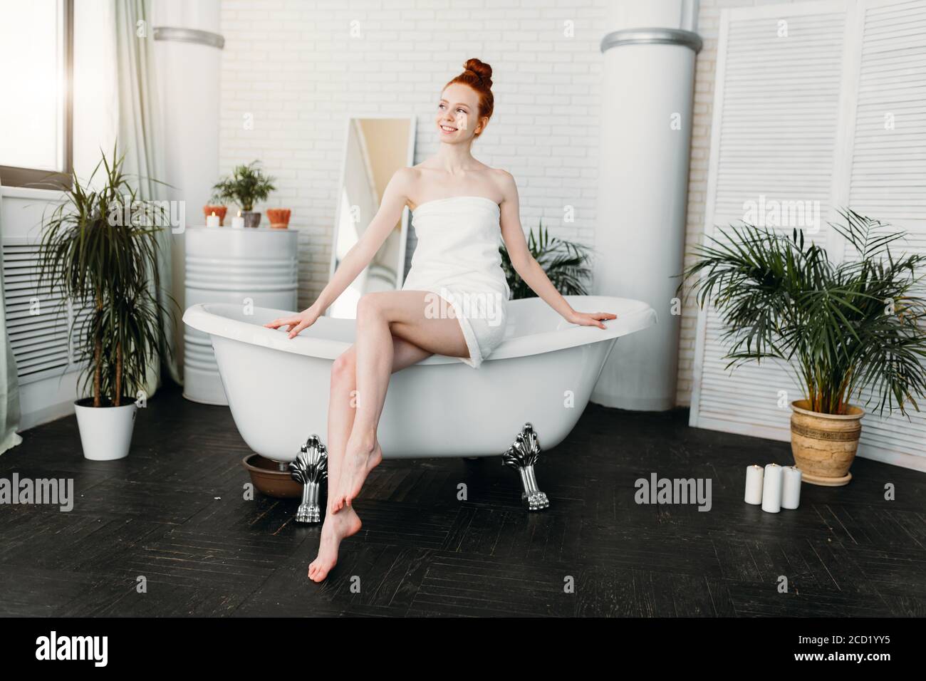Pleasant looking redhead lady with hair bun feeling hapiness and pleasure after beauty treatments, getting ready to have aroma bath in elegant bathroo Stock Photo